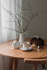 Aesthetic still life - a cup of tea, a teapot, a cosmetic bag, a jug with branches on a round wooden table