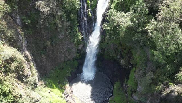 Video a&eacute;reo de una cascada cayendo al arrollo rodeada de &aacute;rboles verdes, de abajo hacia arriba, se puede apreciar la bruma que genera la fuerza del agua