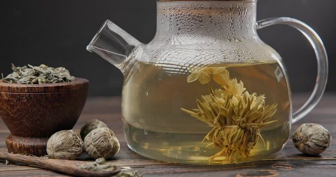 Blooming flower tea ball brewing in a glass teapot with Hot boiling water on wooden background