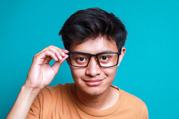 Portrait of Asian man looking at camera while holding his eyeglasses isolated on blue background