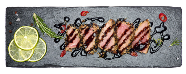 Sliced Organic grilled Tuna fillet covered with sesame seeds on black stone serving board