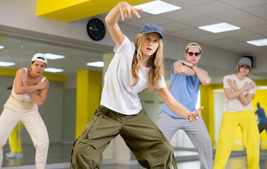 Teen girl in cap rehearses modern dances in dance hall