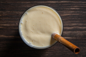 Banana mango smoothie with a bamboo straw on a wooden table, closeup, top view