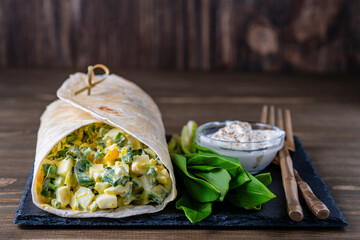 Homemade burrito wraps with boiled eggs, green wild garlic and sour cream for healthy breakfast on wooden board, closeup - 787811106