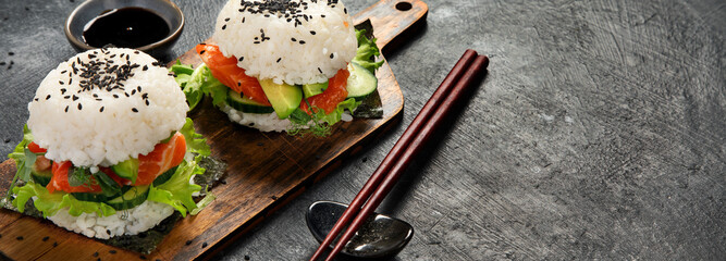 Asian sushi burger, soy sauce, chopstick on dark background. Trendy hybrid food