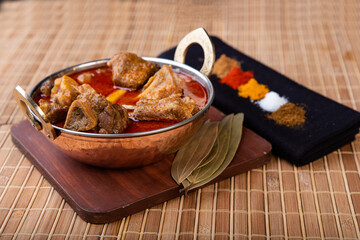 Goan, malvani and konkani style mutton gravy presented in a copper vessel with mutton chop pieces.