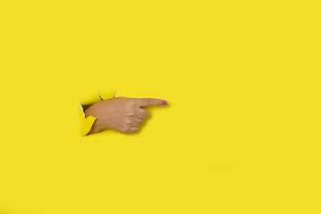Female hand coming out of a hole in a yellow torn paper background pointing to the right.
