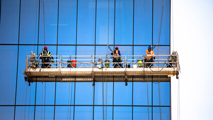 Straight on shot of three window washers on a hanging scaffold on a commercial building with blue...