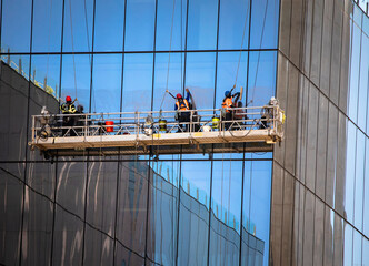 Side and corner view shot of three window washers on a hanging scaffold on a commercial building...