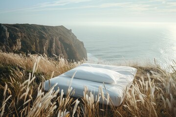 A minimalist bed with a single white pillow, set on a cliff top over a sea of grass waving in the...