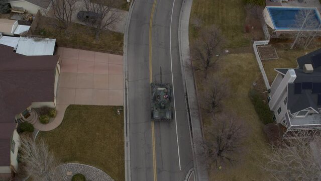 Old tank traveling down neighborhood road - High, drone shot