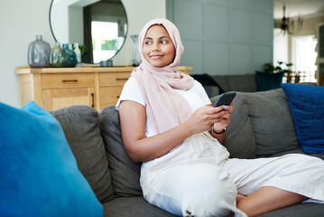 Muslim, woman and sofa on cellphone with smile in living room for break, leisure and network or...
