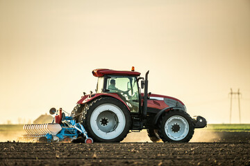 Farmer operates a red tractor, seeding the field against the backdrop of a setting sun