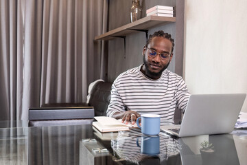 Young African American businessman spends his free time working from home on his laptop.