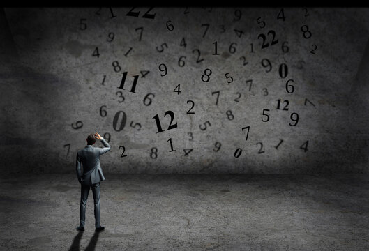 man in suit inside a grey concrete room with numbers on a wall