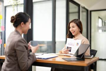 Engaged businesswoman presenting a colorful financial report during a collaborative meeting with a coworker in an office.