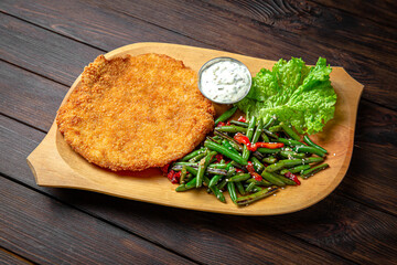Chicken schnitzel in breading with green beans on dark boards background. Menu for a pub