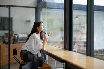 Pensive businesswoman holding a pen, deep in thought as she gazes out of a large window in a...