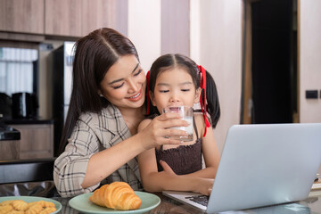 A young single mother receives a snack and eats it with her daughter while she works at home on her laptop.