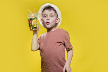 Cute boy in panama drinking mojito cocktail from plastic cup over yellow studio background