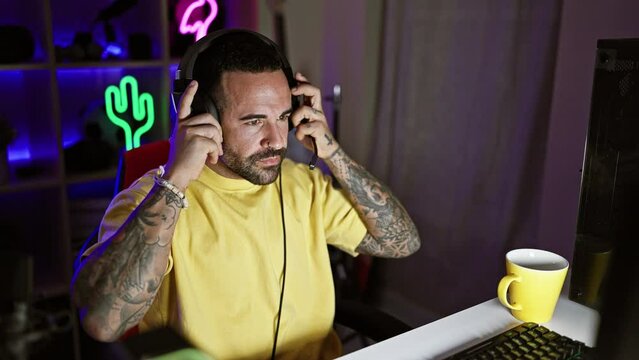 Handsome bearded man wearing headphones in a dark gaming room with neon lights at night.