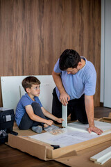Father and son assemble new furniture on floor of new apartment, concept of experience and training.
