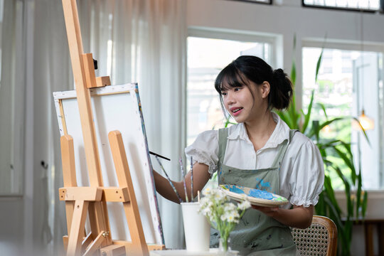 An artistic girl paints with acrylic paints on canvas with determination.