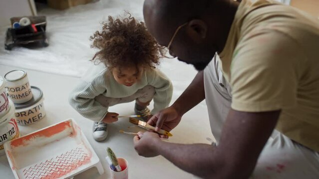High angle footage of African American father explaining to little Biracial daughter what brush to use while renovating room, girl helping dad