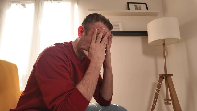 Man with headache sitting on a sofa at home.	
