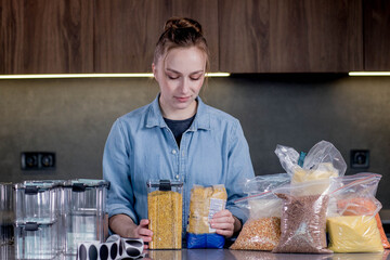 A woman uses containers to organize food in the kitchen. Layout and sorting of food products. Management of the organization in the interior of a modern kitchen. 