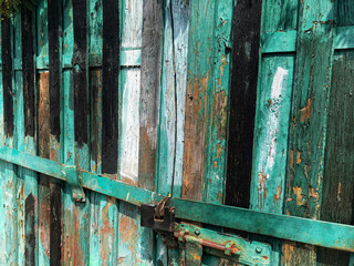 Old painted wooden gate with metal hardware and padlock with peeling paint

