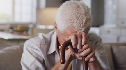 Sofa, cane and sad senior man with depression, grief or loss in living room of nursing home. Mental...