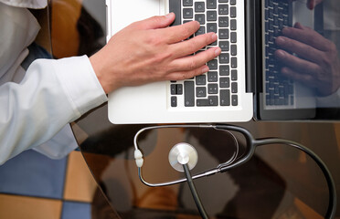 Doctor with a laptop and stethoscope typing a document. Top view