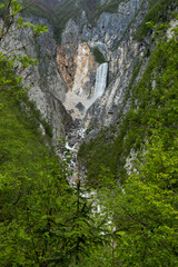 Boka waterfall in Slovenia, near Bovec. Easy trekking nature trail in the forest with the view of the immense waterfall overhanging the mountains visible from the road, long exposure photography.