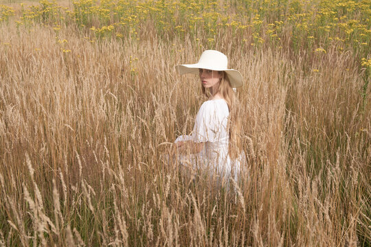 girl in white dress with sun hat sitting in summer grain field