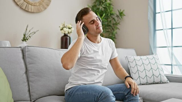 A young man enjoying music with headphones in a cozy living room, showcasing relaxation and modern lifestyle