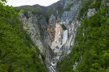 Boka waterfall in Slovenia, near Bovec. Easy trekking nature trail in the forest with the view of the immense waterfall overhanging the mountains visible from the road, long exposure photography.