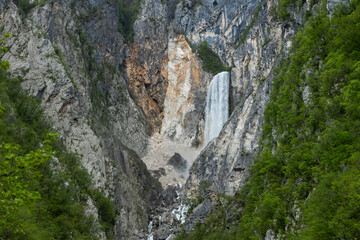 Boka waterfall in Slovenia, near Bovec. Easy trekking nature trail in the forest with the view of the immense waterfall overhanging the mountains visible from the road, long exposure photography.
