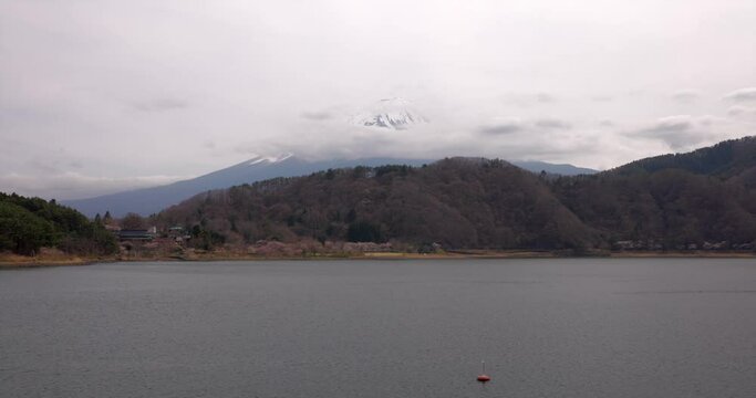 雲に覆われた富士山を背景に湖をボートが通過する風景。