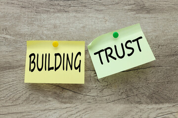 Build trust two stickers, green and yellow, riveted to a wooden background. text