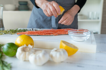 Woman is seasoning and marinating a half salmon fillet with lemon juice on a cutting board
