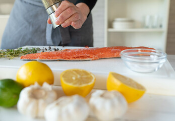 Person seasoning a raw half salmon fillet with a pepper shaker on a cutting board