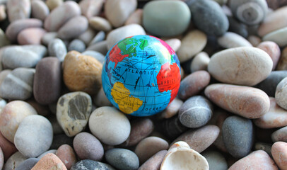 Miniature globe on a sea stones with conventionally drawn continents, oceans and trade routes on it
