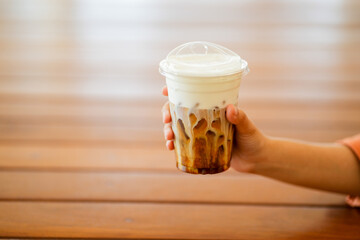 Close up and selective focus hand of woman holding a take-out iced espresso with cream foam at...