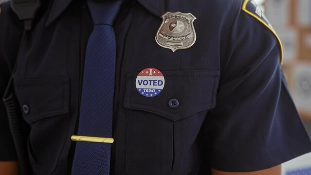African american male police officer attaching 'i voted' sticker on uniform indoors
