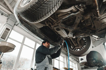 Workman mechanic working under car in auto repair shop