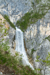 Boka waterfall in Slovenia, near Bovec. Easy trekking nature trail in the forest with the view of the immense waterfall overhanging the mountains visible from the road, long exposure photography.