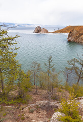 Baikal Lake in May. View of the shore of Olkhon Island with green larches, the famous Shamanka Rock - natural landmark of the lake, and ice drift in the Small Sea. Spring landscape. Natural background