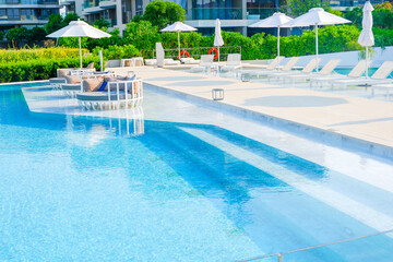 Empty swimming pool with sunbed and white umbrella in resort hotel for vacation leisure and white...