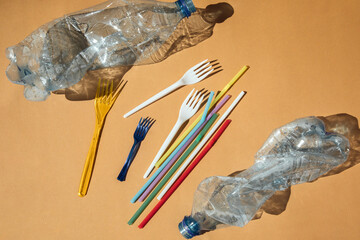 Crumpled empty transparent plastic bottles from water, plastic forks and straws on a brown...